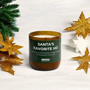 Candle labeled 'Santa's Favorite Ho' with Christmas decorations on a white background
