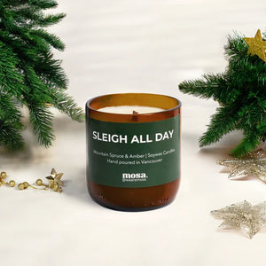 Candle labeled 'Sleigh All Day' with Christmas decorations on a light background