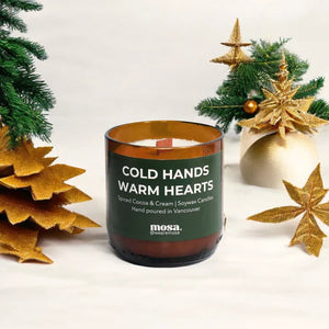 Candle with 'Cold Hands Warm Hearts' text surrounded by Christmas decorations on a white background