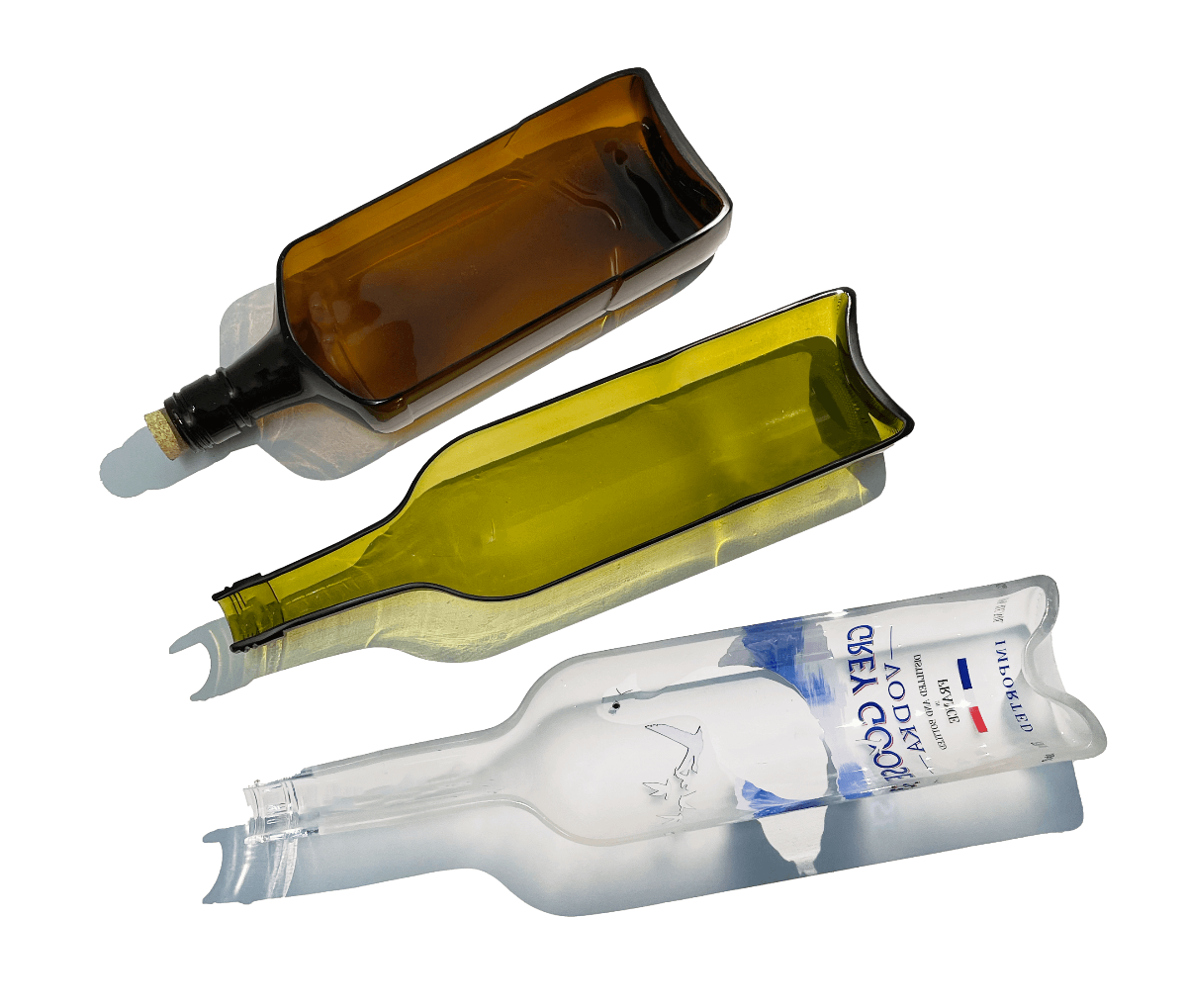 Three flattened glass bottles repurposed into serving platters—one amber brown, one olive green, and one clear bottle with a visible vodka label—arranged diagonally on a transparent background, showcasing their upcycled, eco-friendly design.