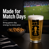 Beer glass with FIFA Vancouver logo on a table with snacks and sports event in the background