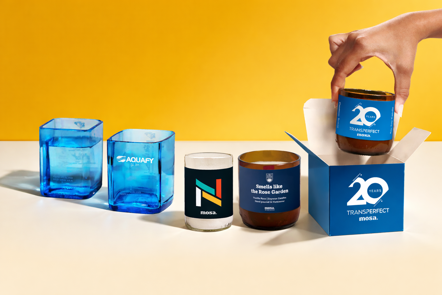 Collection of branded glassware containers with a hand placing one into a box on a yellow background