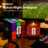 FIFA World Cup collectible candle and packaging on a table with a soccer game in the background.