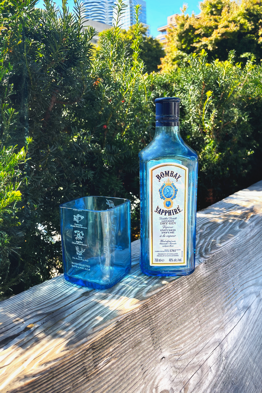 Bottle of Romelie Sapphire gin with a custom glass on a wooden surface outdoors