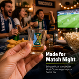 People celebrating in a living room with a TV showing a sports game, holding a shot glass with FIFA World Cup branding.