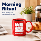 Red mug with 'WE ARE 26 VANCOUVER' text on a table with coffee and croissant, featuring the text 'Morning Ritual'.