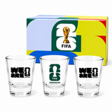Set of three shot glasses with FIFA branding in front of a colorful box.