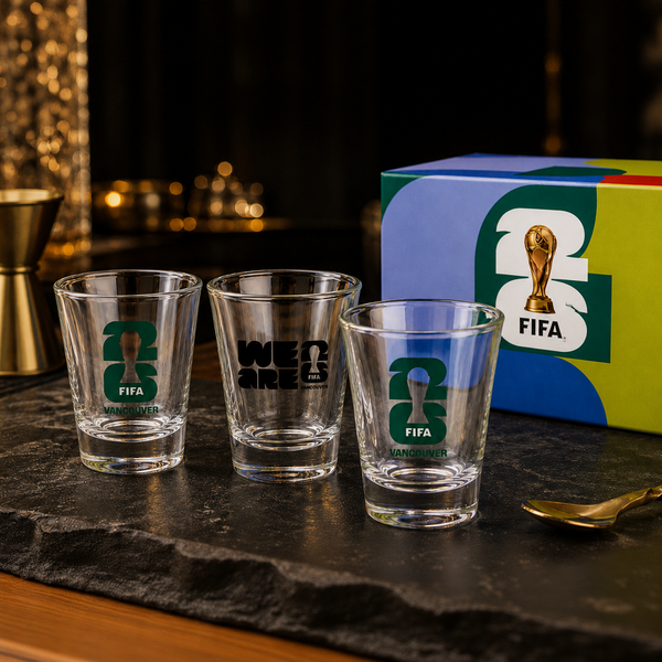 Three shot glasses with FIFA branding on a dark surface with a colorful box in the background.