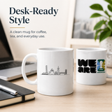 Two white mugs on a desk with one featuring a city skyline design and the other displaying 'WE ARE VANCOUVER'.