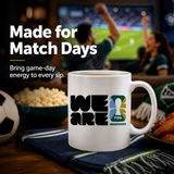 White mug with FIFA Vancouver logo on a table with snacks and a TV in the background